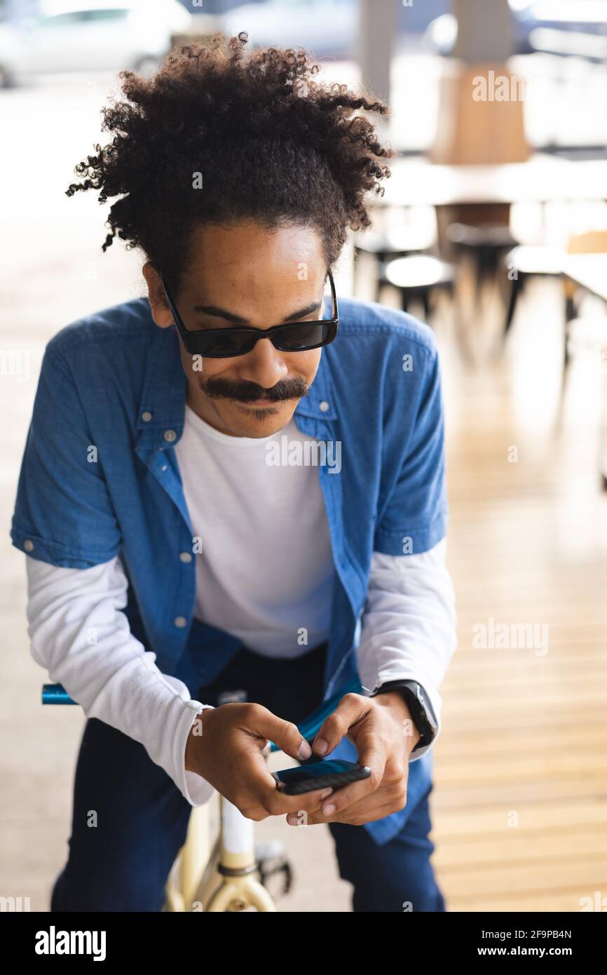 Mixed race man with moustache sitting on bicycle in street using smartphone. digital nomad, out and about in the city. Stock Photo
