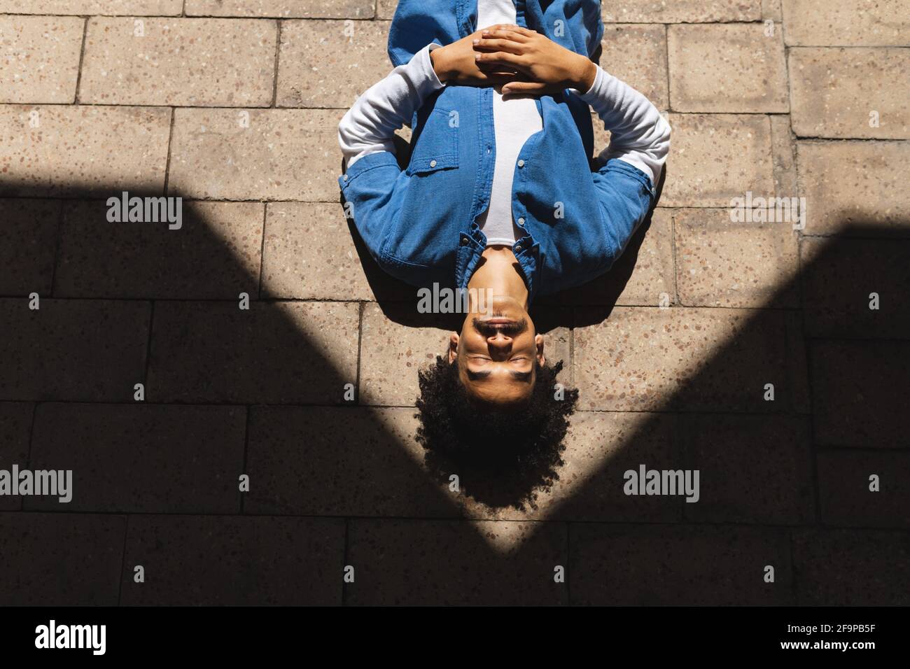 Mixed race male with moustache lying on street with eyes closed and relaxing. green urban lifestyle, out and about in the city. Stock Photo