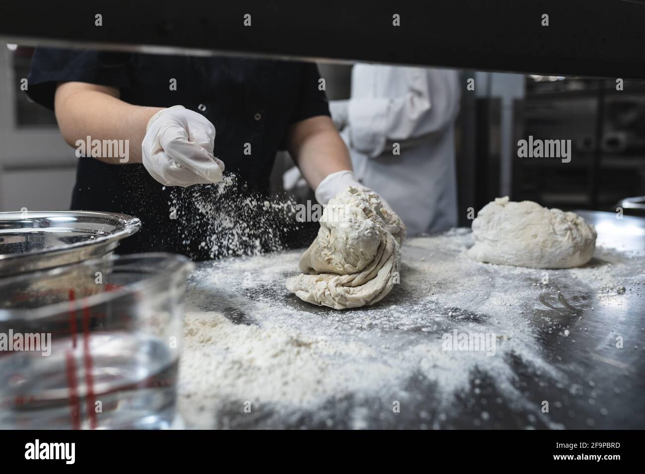 Midsection of professional chef kneading dough wearing sanitary gloves