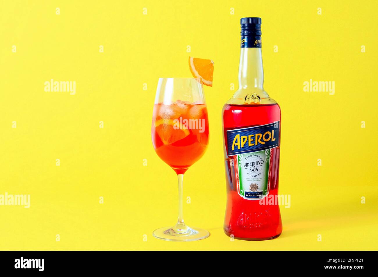 Lugansk, Ukraine - March 29, 2021: Aperol Spritz Cocktail. Aperol in bottle and wine glass with ice on yellow background. Long fizzy drink. Minimal cr Stock Photo