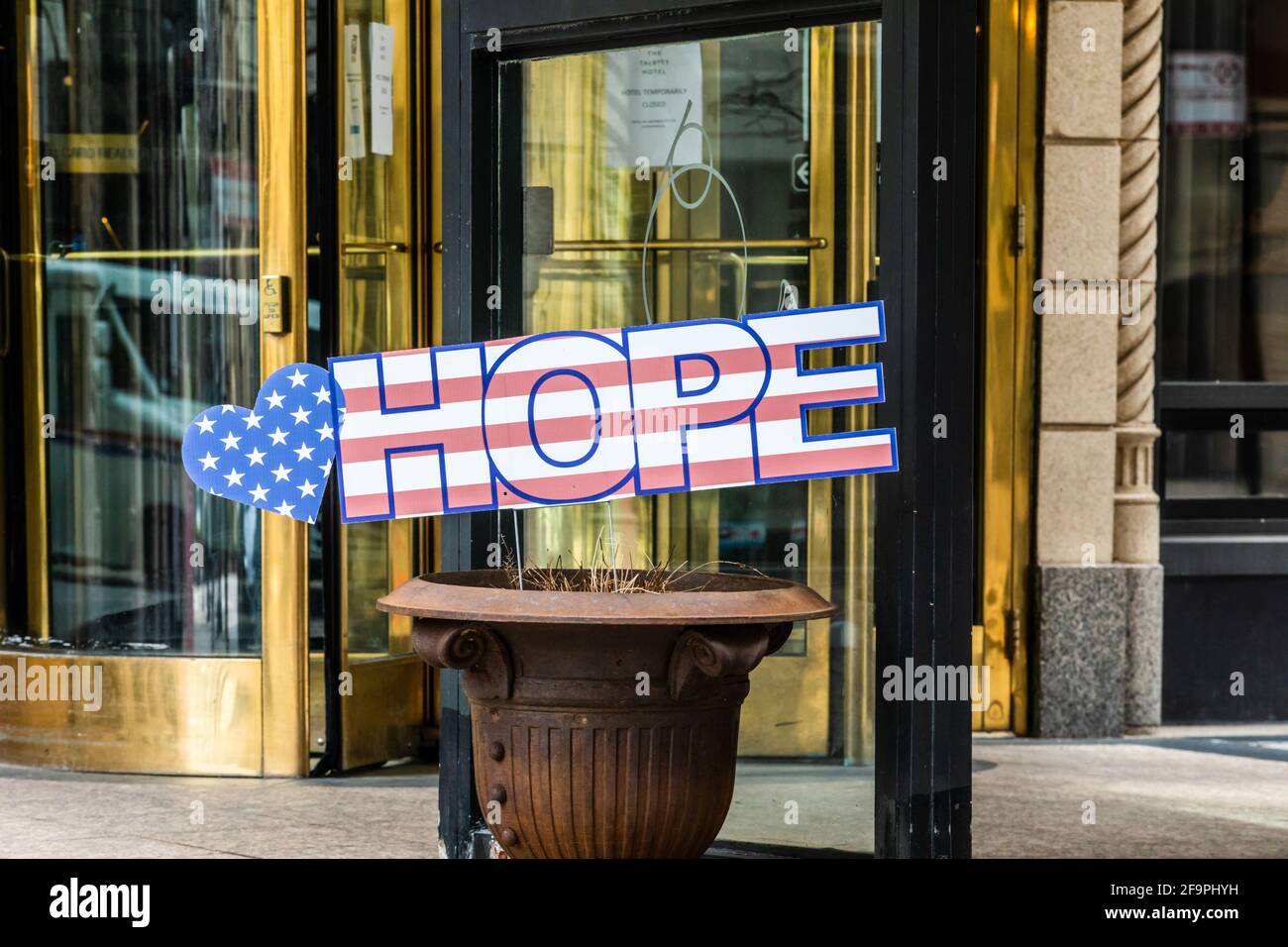 The word Hope with a US Flag background, written on cardboard board being displayed in a city sidewalk planter. Stock Photo