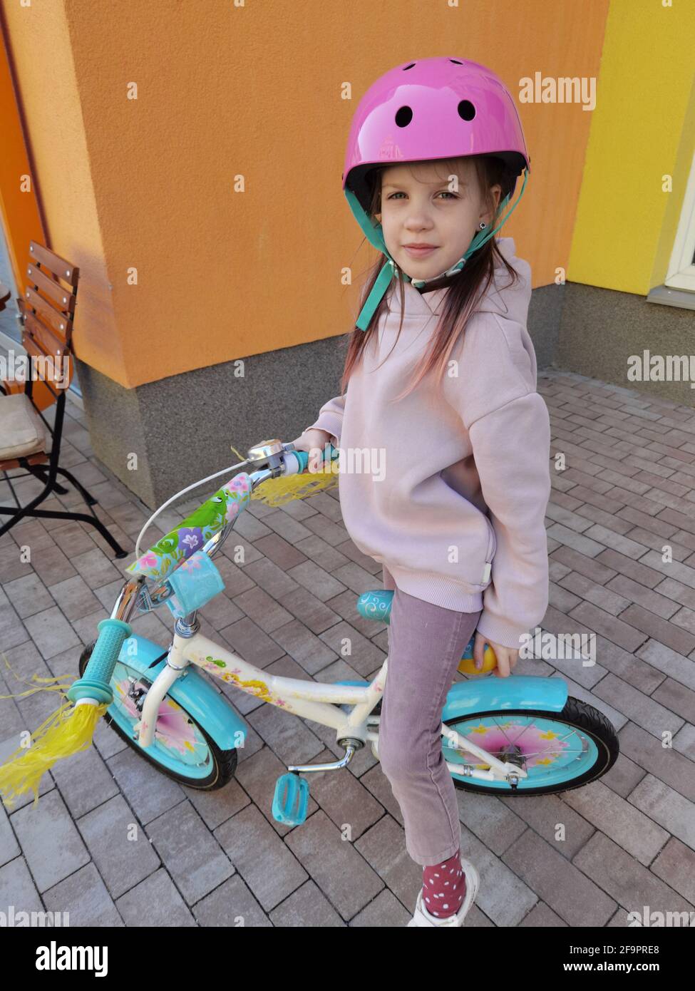 Portrait of a playful funny girl in a pink safety helmet on her bike