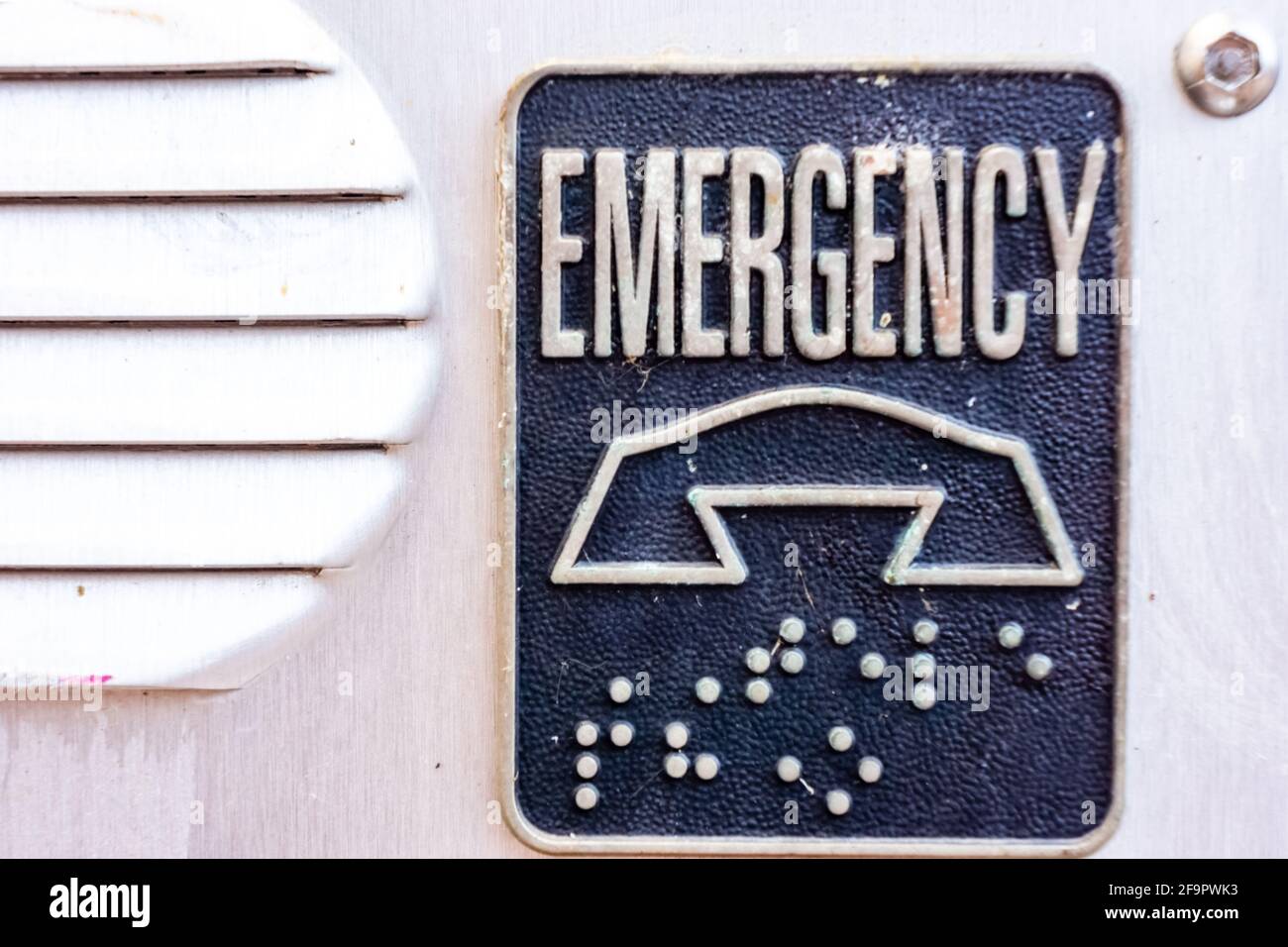 Close up of an emergency call box placard showing the word emergency a graphic of a phone and braille lettering. Stock Photo