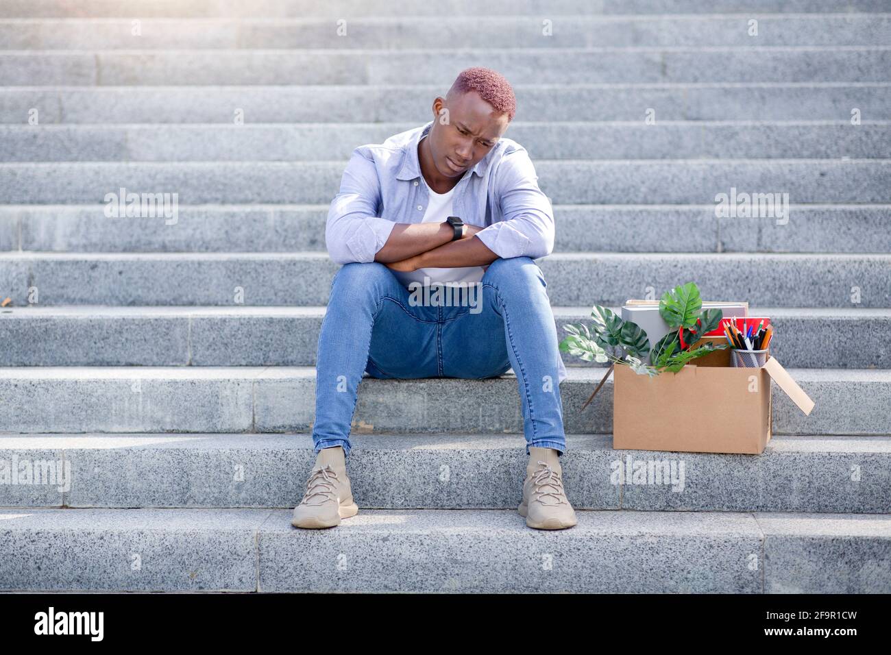 Bankruptcy and unemployment. Stressed black guy with personal stuff feeling upset after losing work on stairs outside Stock Photo
