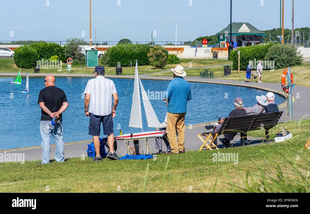 Group of senior elderly men socialising with radio controlled yachts & boats at the Oyster Pond boating lake in Littlehampton, West Sussex, UK. Stock Photo