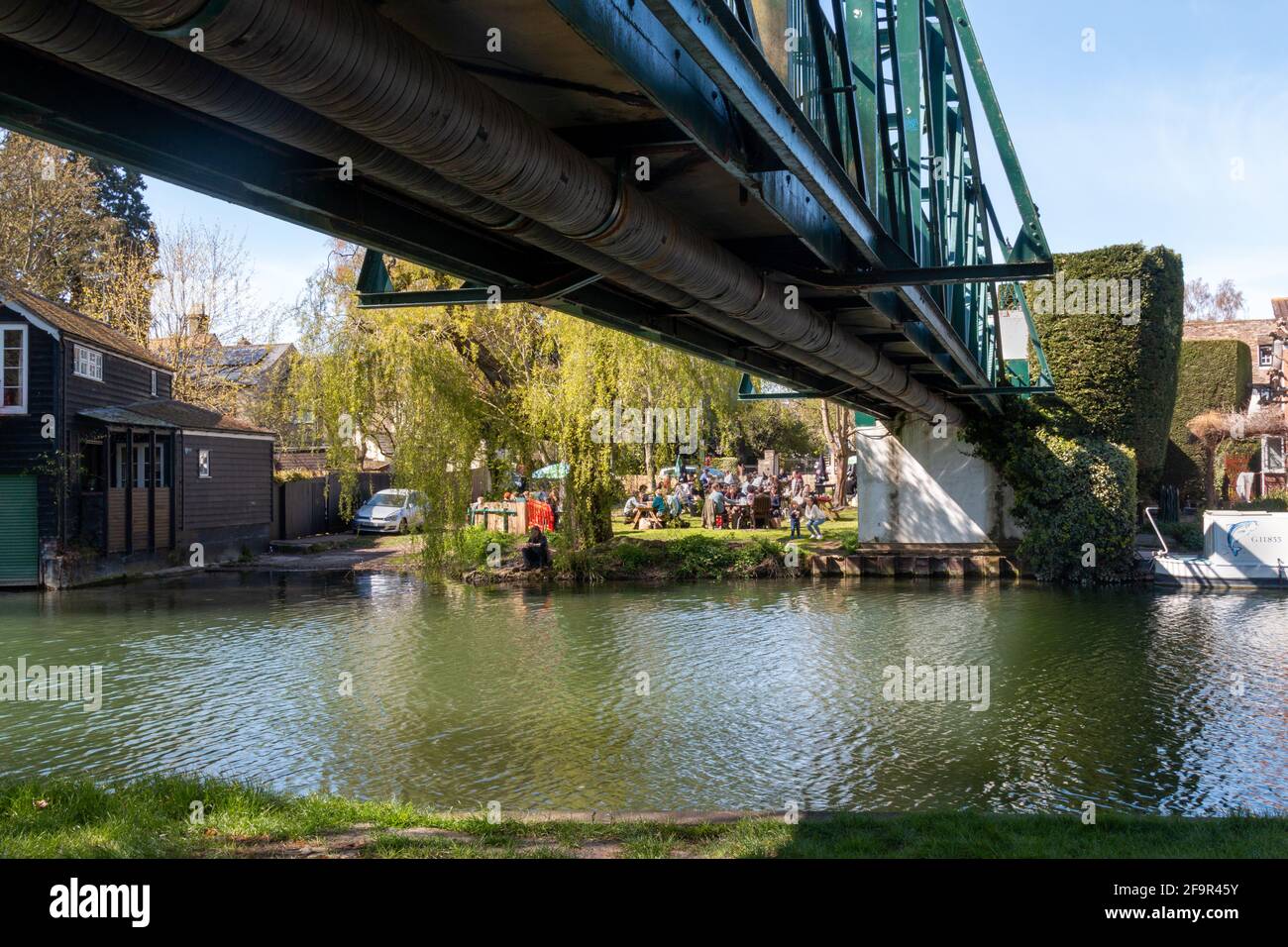 A view from Stourbridge Common across the river, under the bridge, to the busy  garden at the Green Dragon Pub on a sunny day. Cambridge, UK Stock Photo