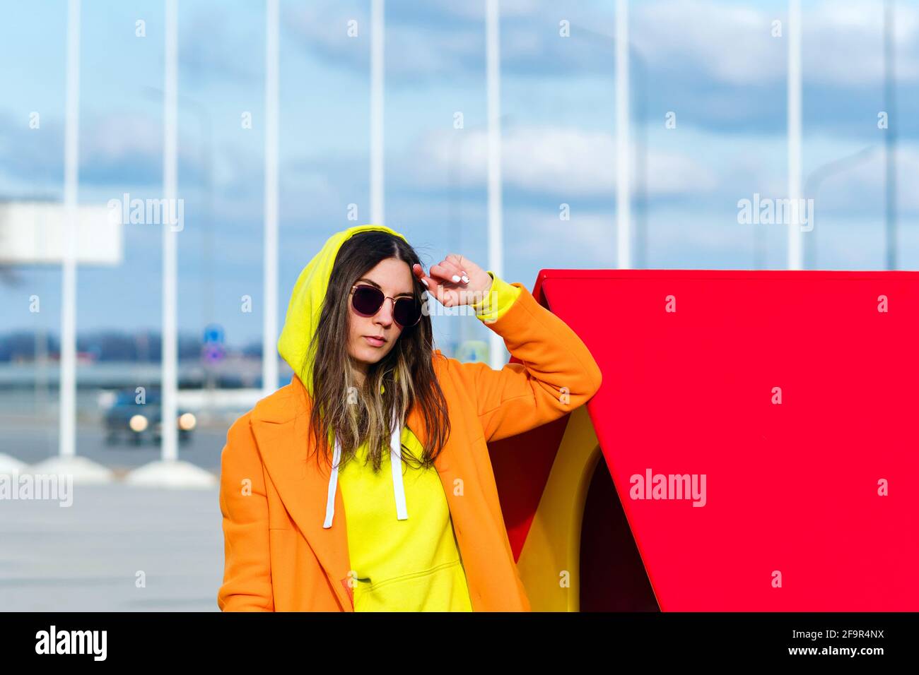 Millennial Hipster Girl in lilac sunglasses, orange coat, yellow