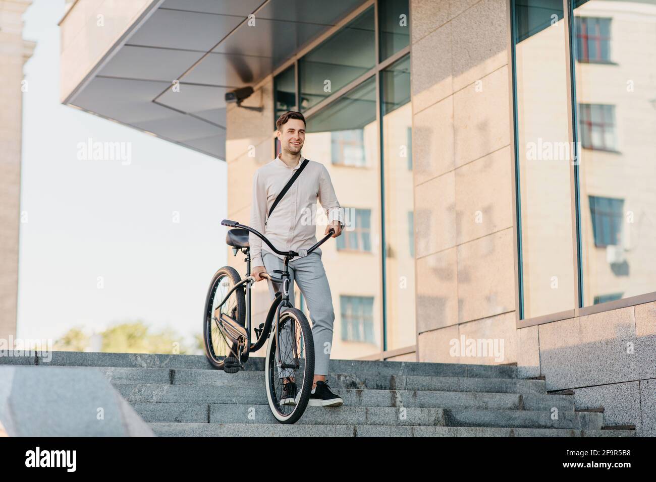 Confident young businessman walking with eco transport on street in town, going to work and active lifestyle Stock Photo