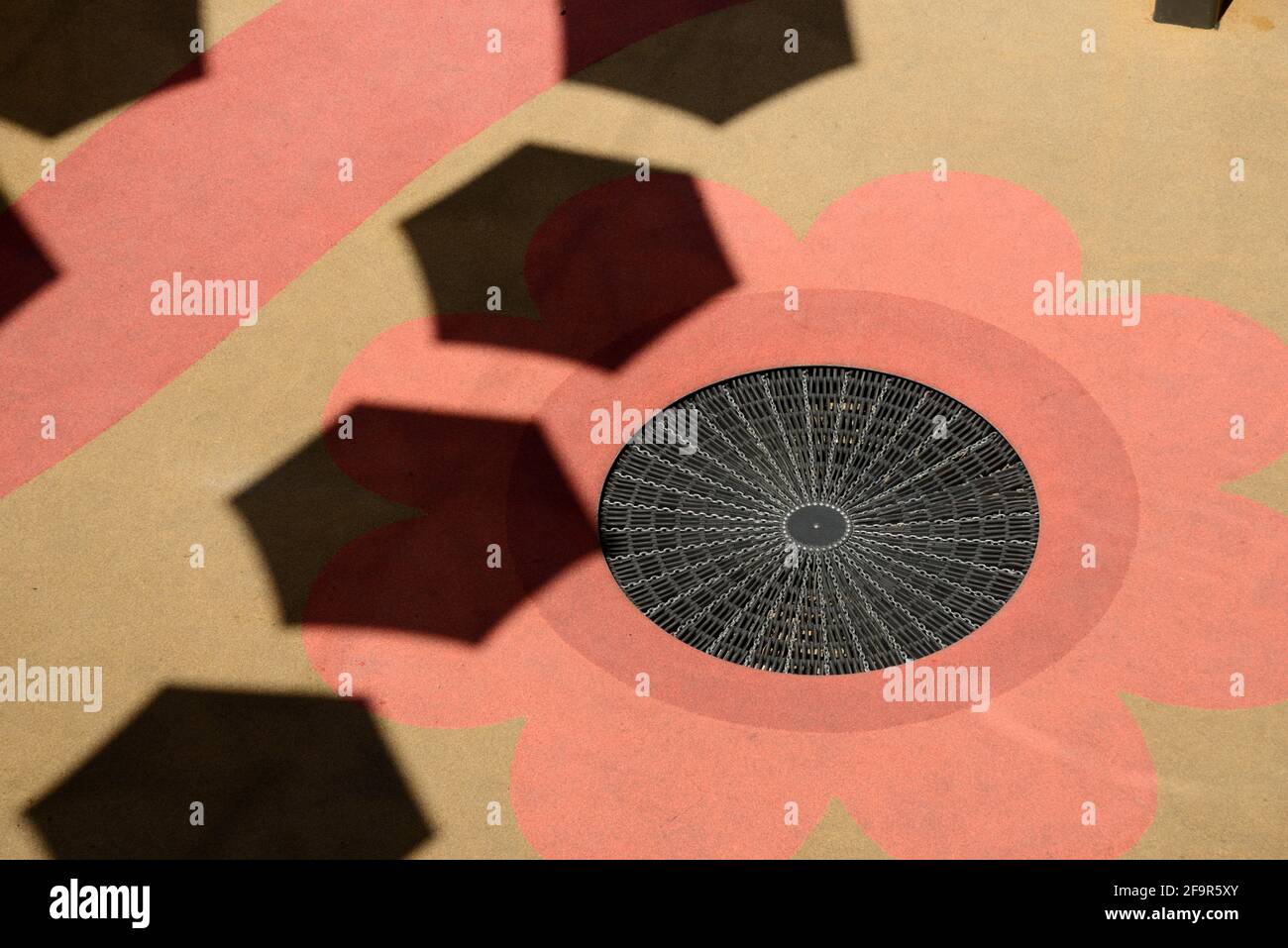 Abstract Street Patterns on Pavement with Decorated Sewer Cover, Manhole Cover or Drain Cover Disguised as Pink Flower & Shadows of Parasols France Stock Photo