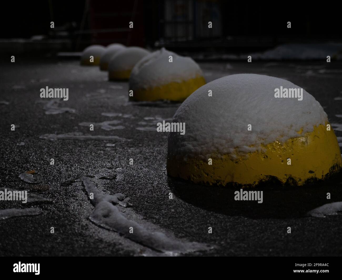 Yellow concrete anti-parking hemisphere-shaped bollards covered by snow and ice.  Roadside on a winter night. Stock Photo