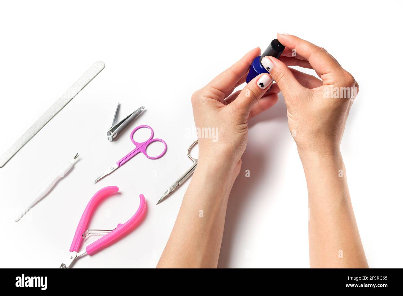 Female hands paint nails, next to lay down devices for nail care. The girl does a manicure. on white background. View from above.  Stock Photo