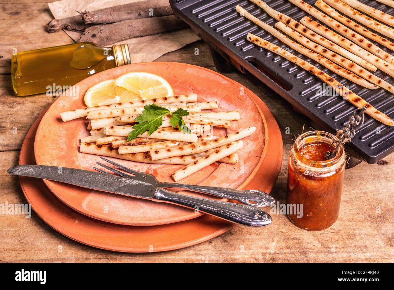 Grilled scorzonera with sauce. Cutlery, rustic ceramic plates, grill