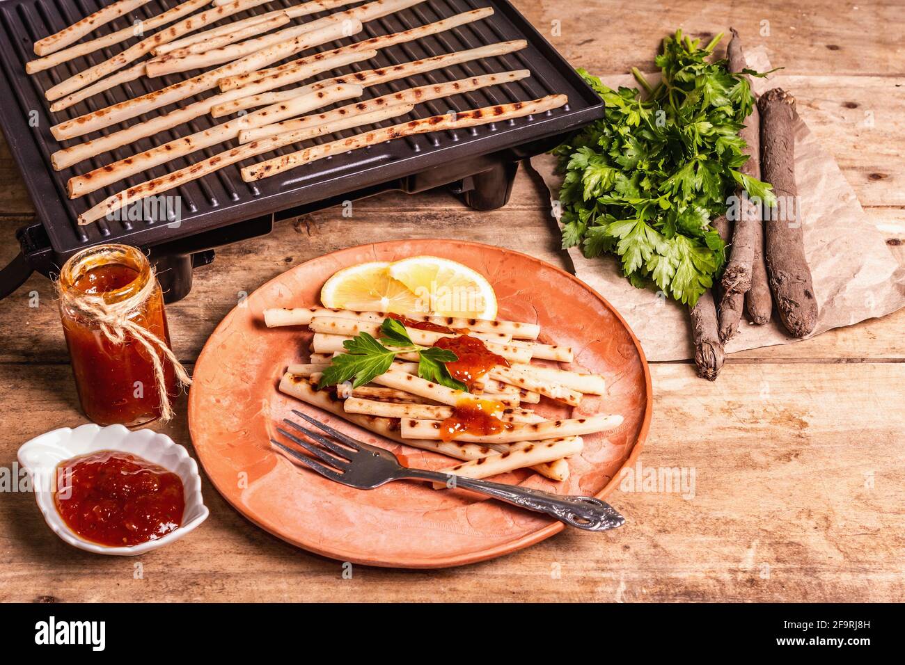 Grilled scorzonera with sauce. Cutlery, rustic ceramic plates, grill