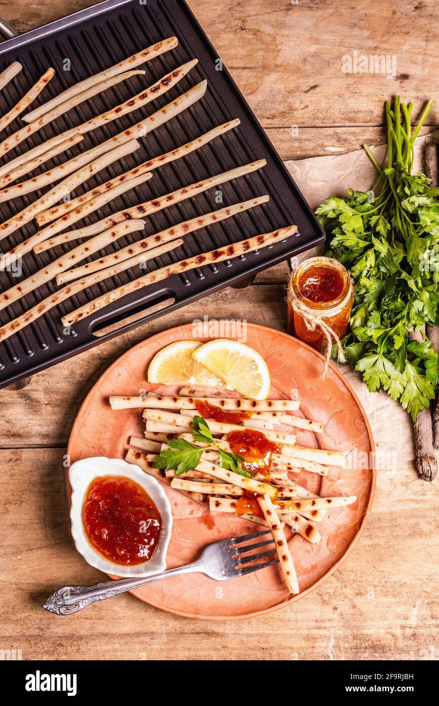 Grilled scorzonera with sauce. Cutlery, rustic ceramic plates, grill