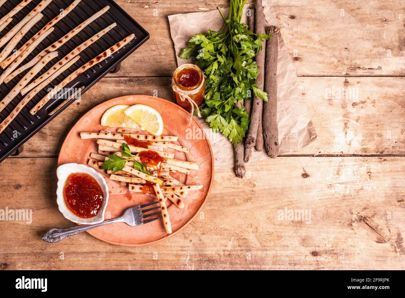 Grilled scorzonera with sauce. Cutlery, rustic ceramic plates, grill