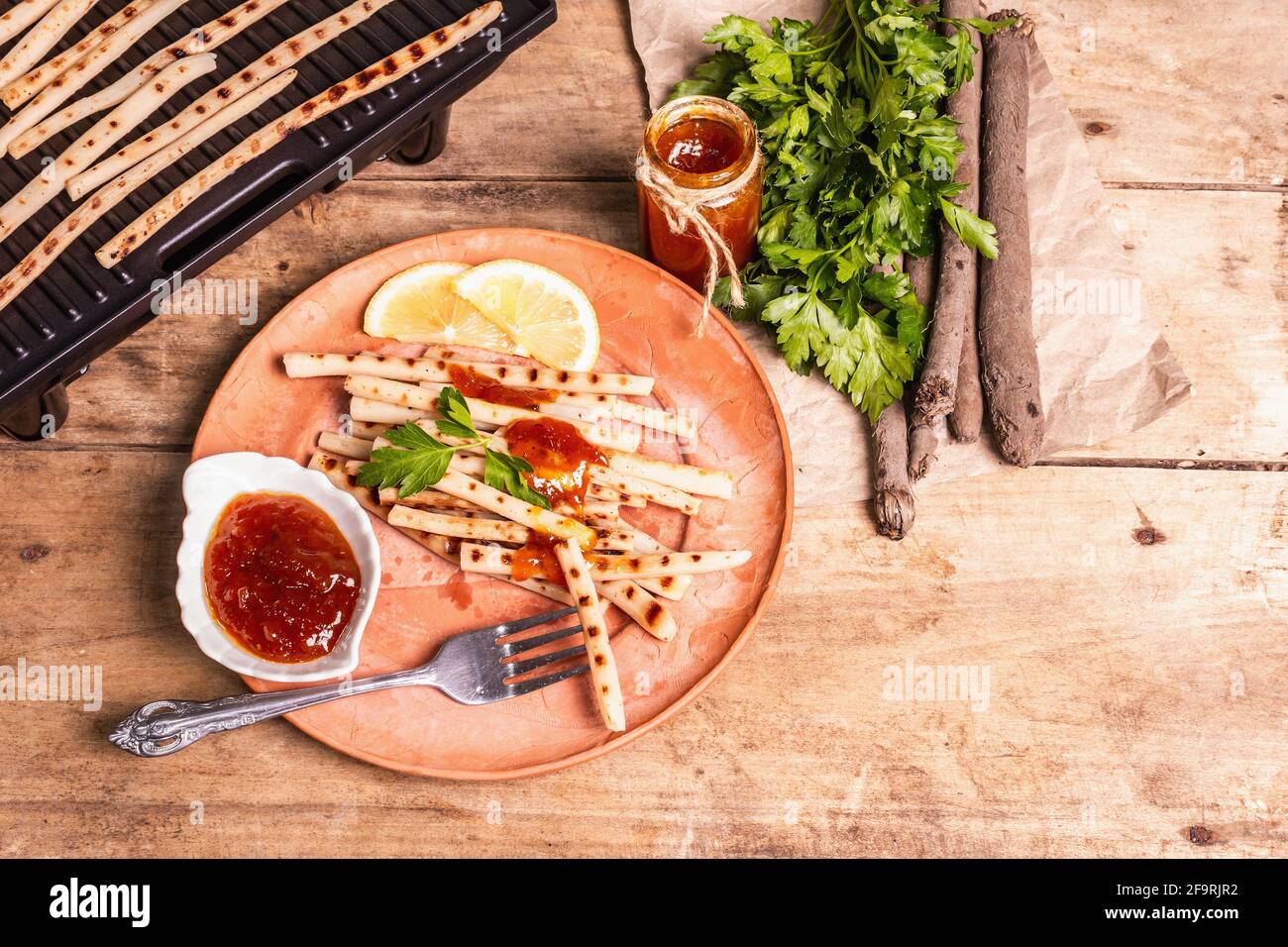 Grilled scorzonera with sauce. Cutlery, rustic ceramic plates, grill