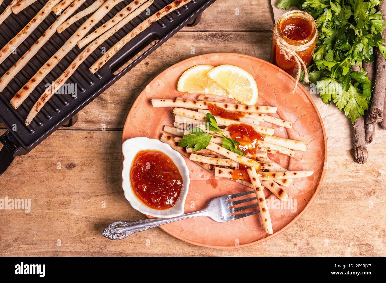 Grilled scorzonera with sauce. Cutlery, rustic ceramic plates, grill