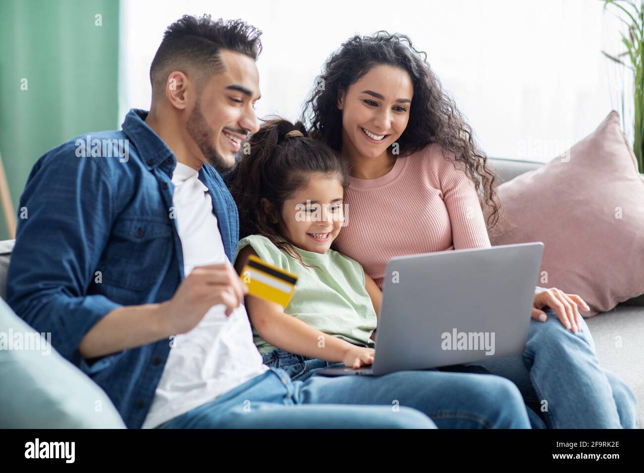 Happy Arabic Parents And Their Little Daughter Making Online Shopping At Home Stock Photo