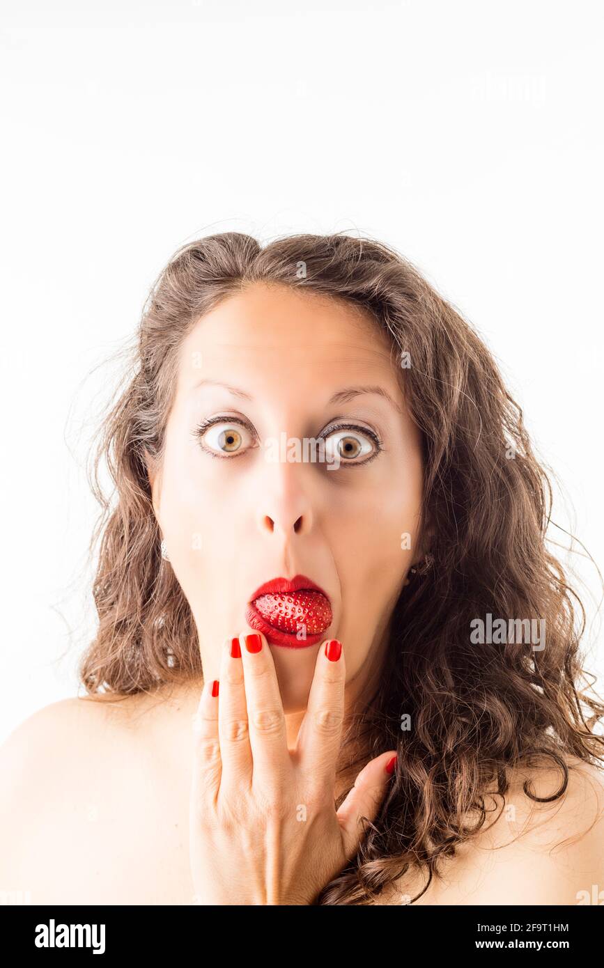 Portrait of a woman with a strawberry in her mouth as a tongue and a hand on her face showing surprise. Stock Photo