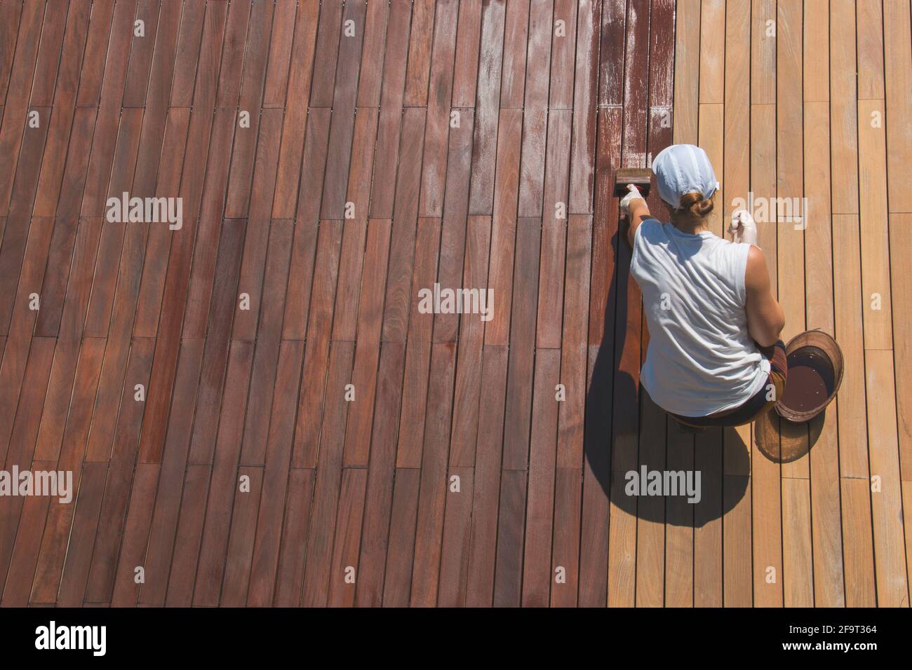 Wood deck renovation treatment, the person applying protective wood stain with a brush, overhead
