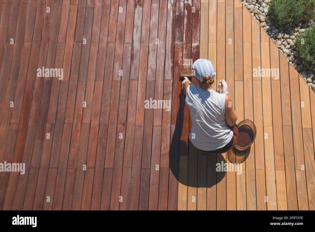 Above view of beautiful garden decking renovation, woman trades worker is oiling a deck, terrace wood deck stain restoration process Stock Photo