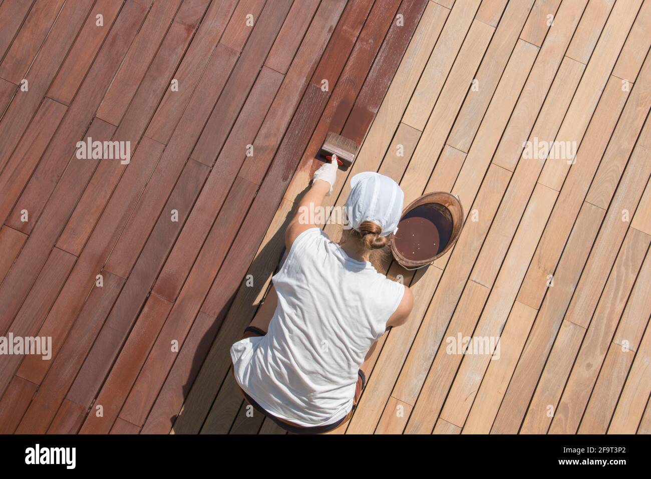 Hardwood deck oiling, decking renovation and nourishing by oil with a brush, overhead view of woman worker renovating wooden terrace Stock Photo
