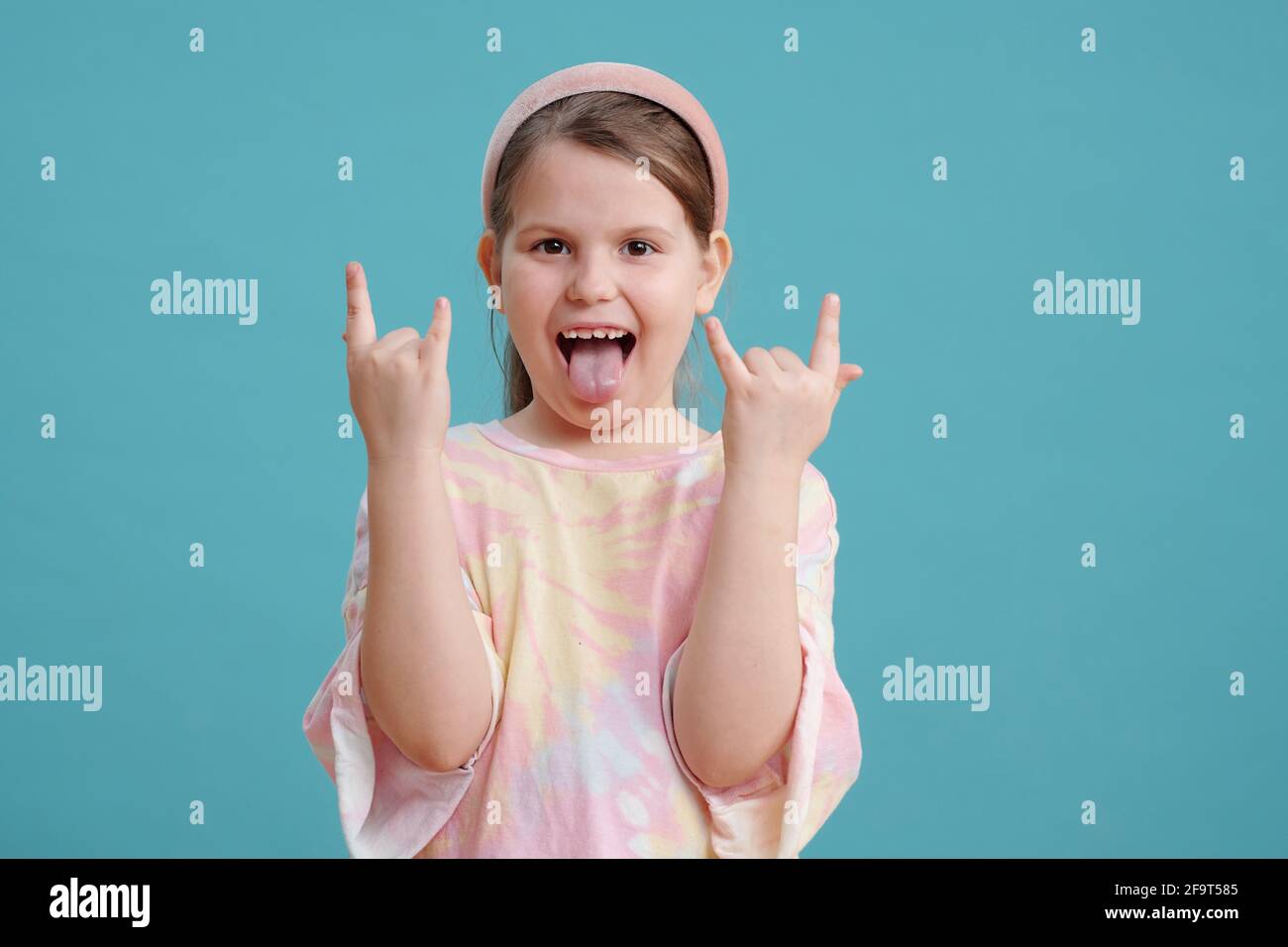 Portrait of funny little girl showing her tongue and posing at camera against the blue background Stock Photo