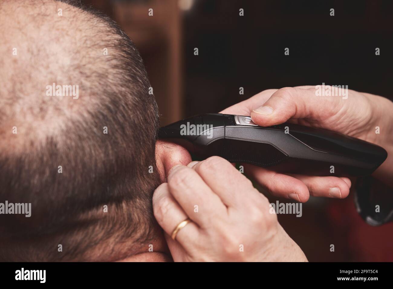 Wife cutting husbands hair at home with a haircut machine or hair clipper. Stock Photo