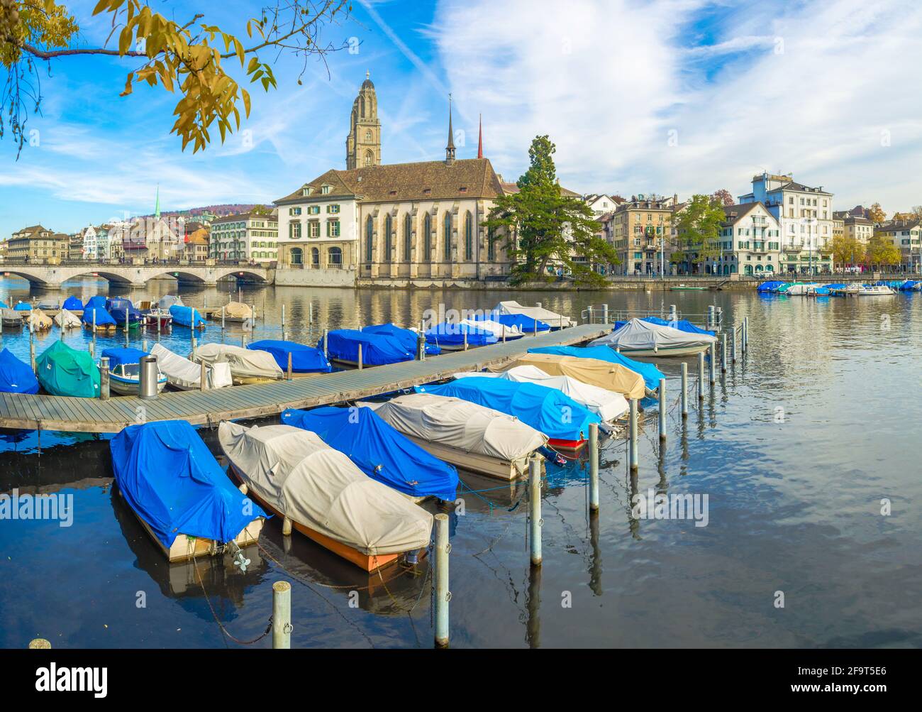 several boats are anchoring on the limmat river in zurich with famous Grossmunster cathedral behind them Stock Photo