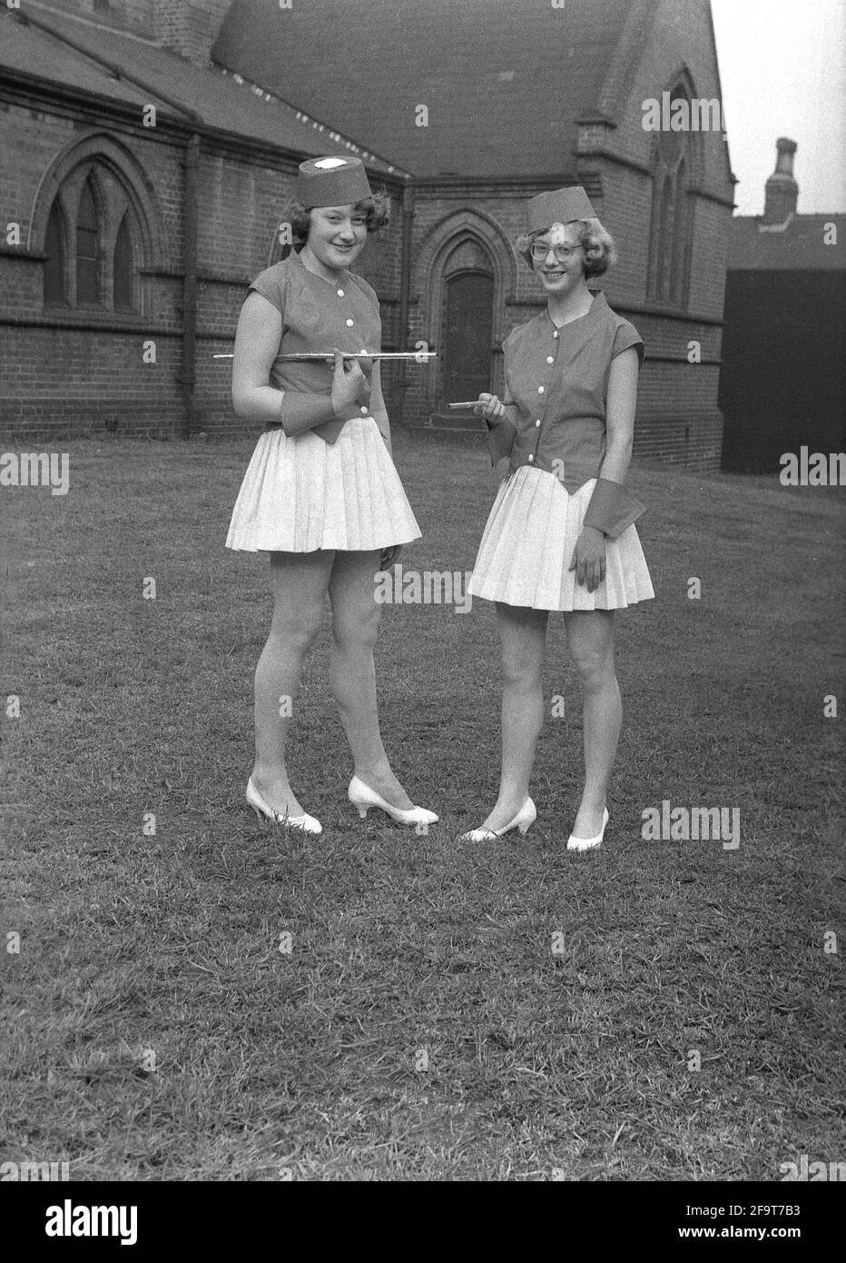 1956, historical, outside in the grounds of church, standing for their photo, two young ladies in their costumes for the traditional May Queen procession, England, UK. In many Englsih villages, the May Day celebrations involved the crowning of a May Queen and dancing around a Maypole, actiitvities that have taken place in England for centuries. Selected from the girls of the area, the May Queen wearing a crown, would start the procession and the parade of floats and dancing. In the industrialised North of England, the Church Sunday Schools often led the organisation of the day. Stock Photo