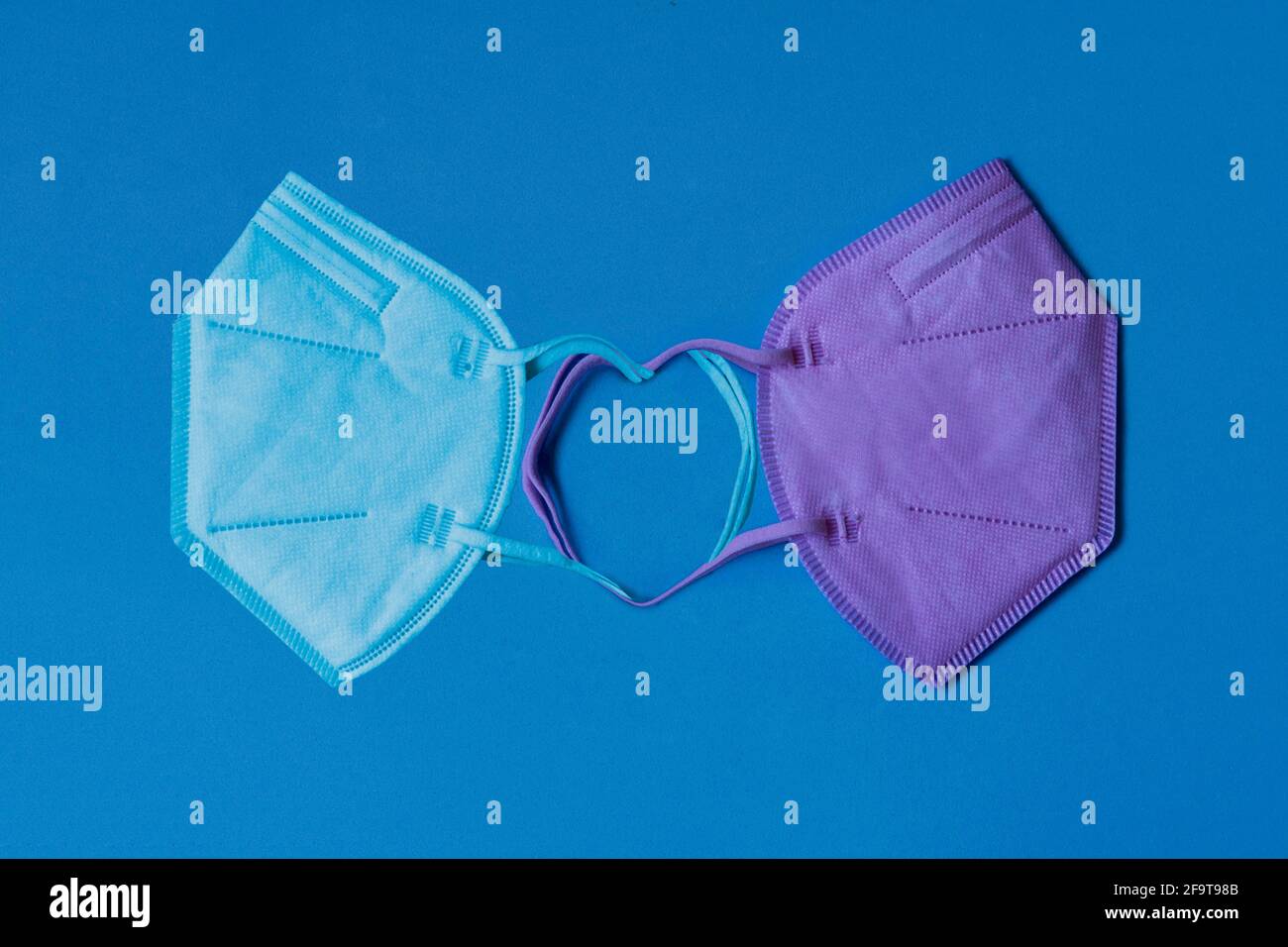 Two pink and blue FFP2 type medical masks forming a 'Stay safe' heart on a blue background Stock Photo