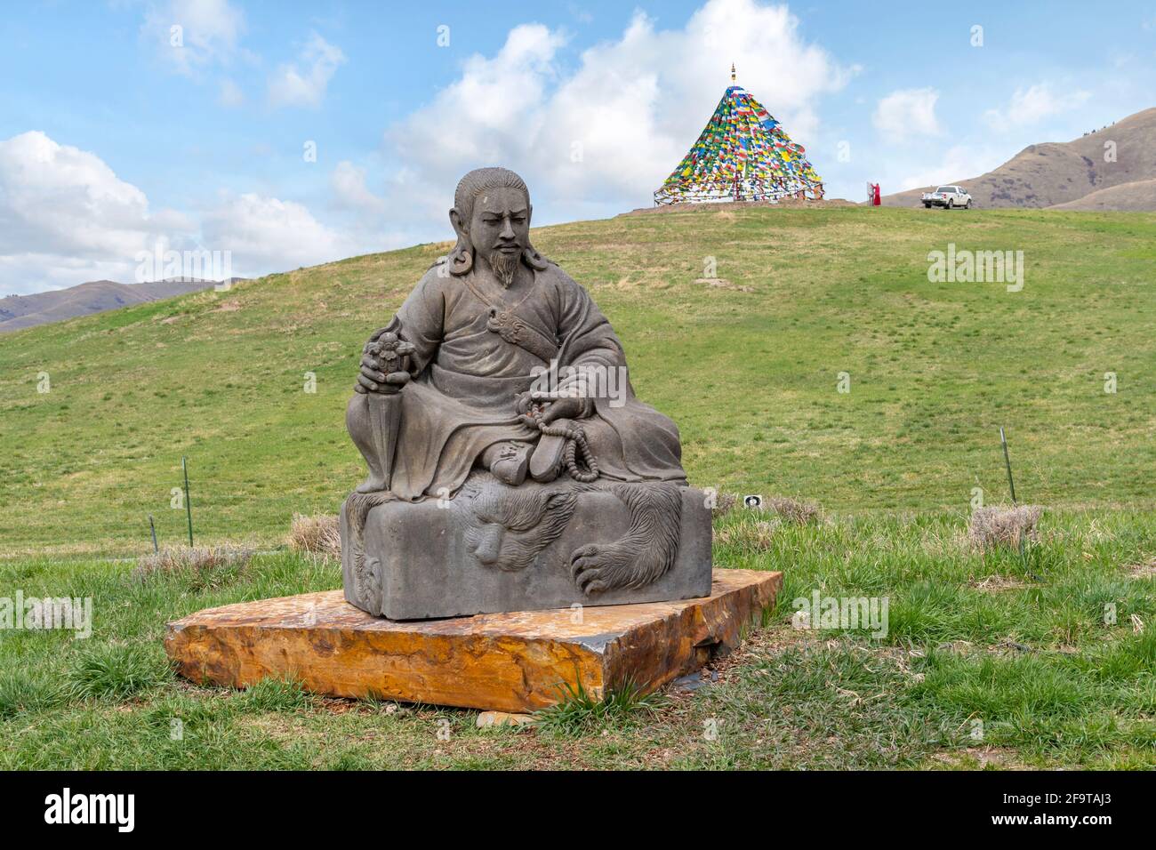 A Buddhist statue of a sitting warrior or king in the rural countryside of Montana, with a teepee made of flags blurred in the distance. Stock Photo