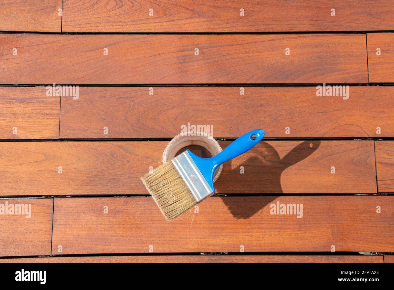 Teak wood deck renovation treatment and maintenance concept, paint brush on the bucket with oil, staining wooden decking Stock Photo