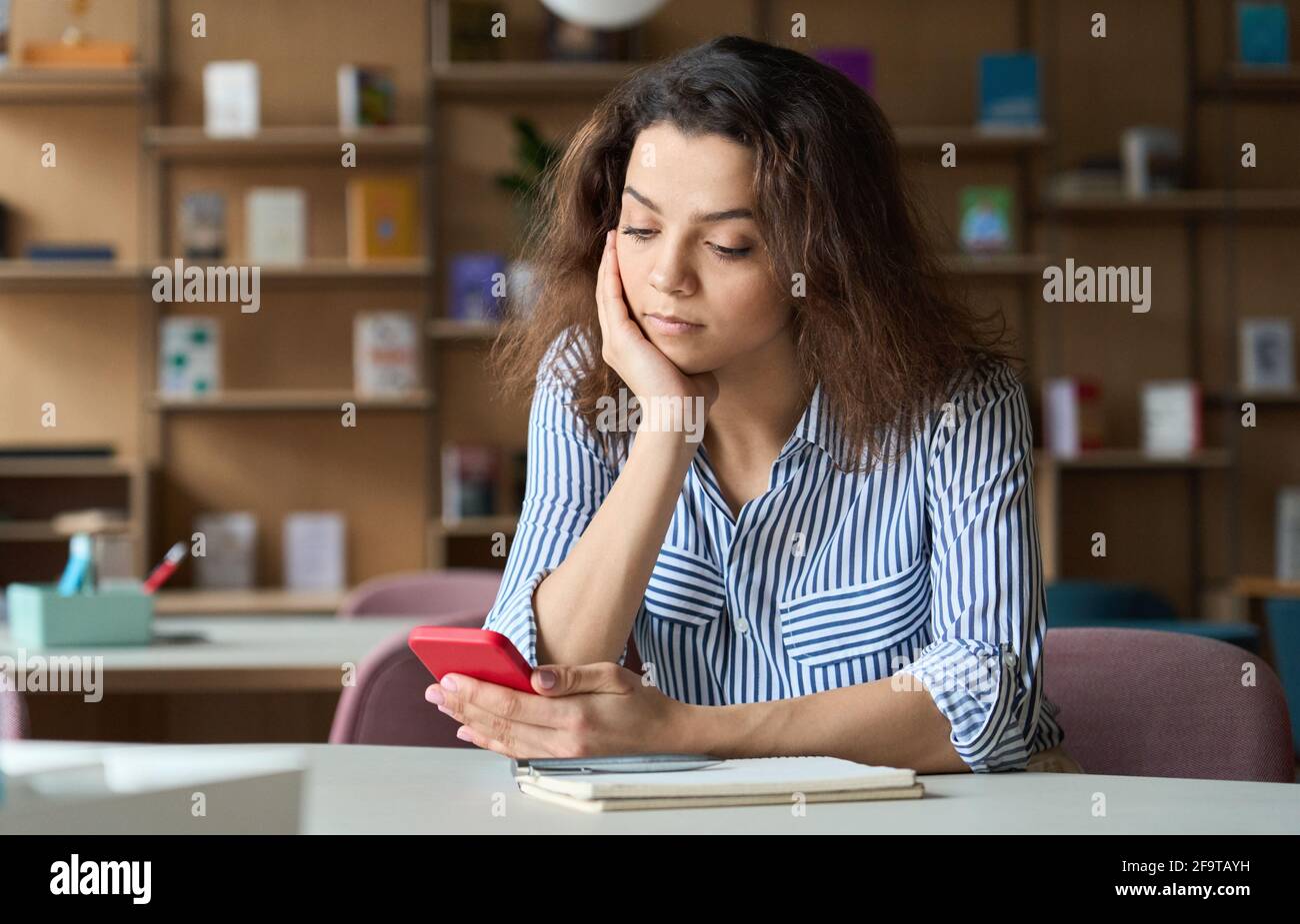 Indian student sitting at table with cellphone using training mobile app. Stock Photo