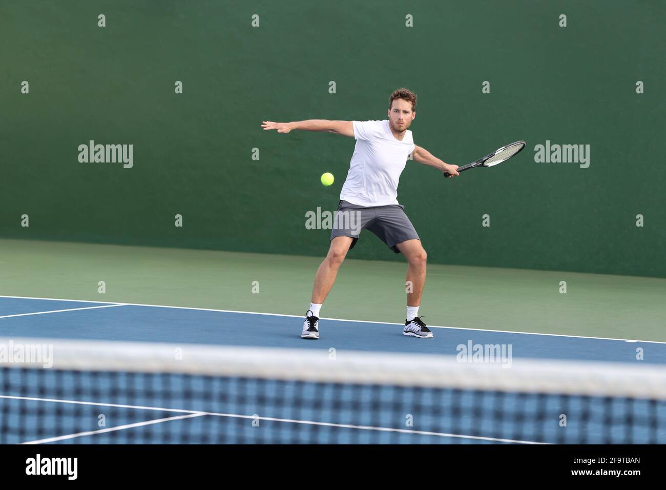 Professional tennis player athlete man focused on hitting ball over net on hard court playing tennis match with someone. Sport game fitness lifestyle Stock Photo