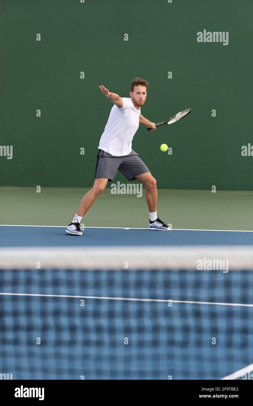 Professional tennis player athlete man hitting forehand ball over net on hard court playing tennis match. Sport game fitness lifestyle Stock Photo