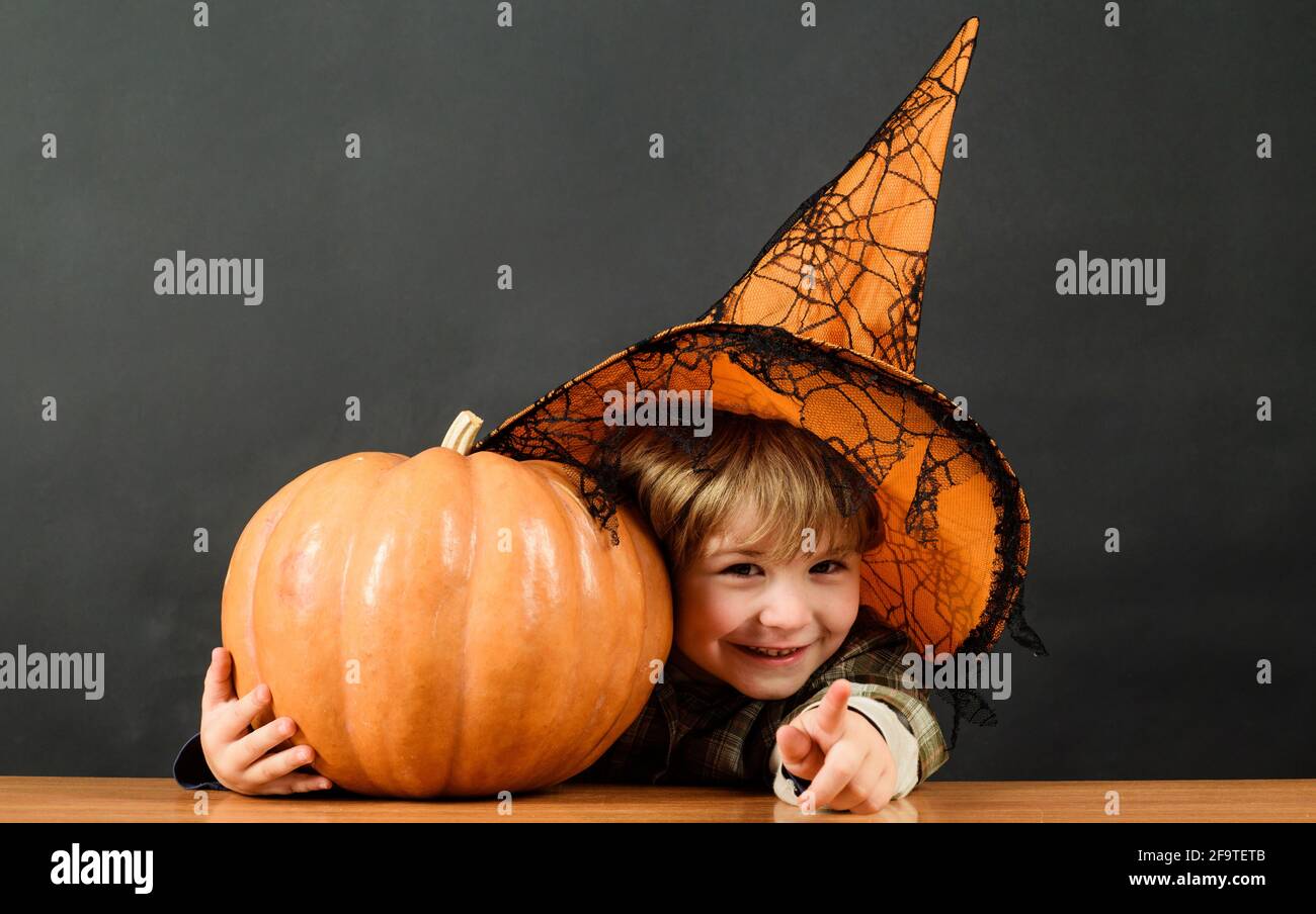 Halloween holiday. Child in witch hat with pumpkin pointing to you. Trick or treat. Stock Photo