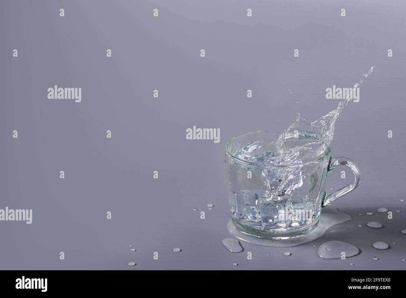 https://c8.alamy.com/comp/2F9TEX0/crystal-clear-water-with-ice-in-a-transparent-glass-cup-on-a-gray-background-splash-and-splash-2F9TEX0.jpg