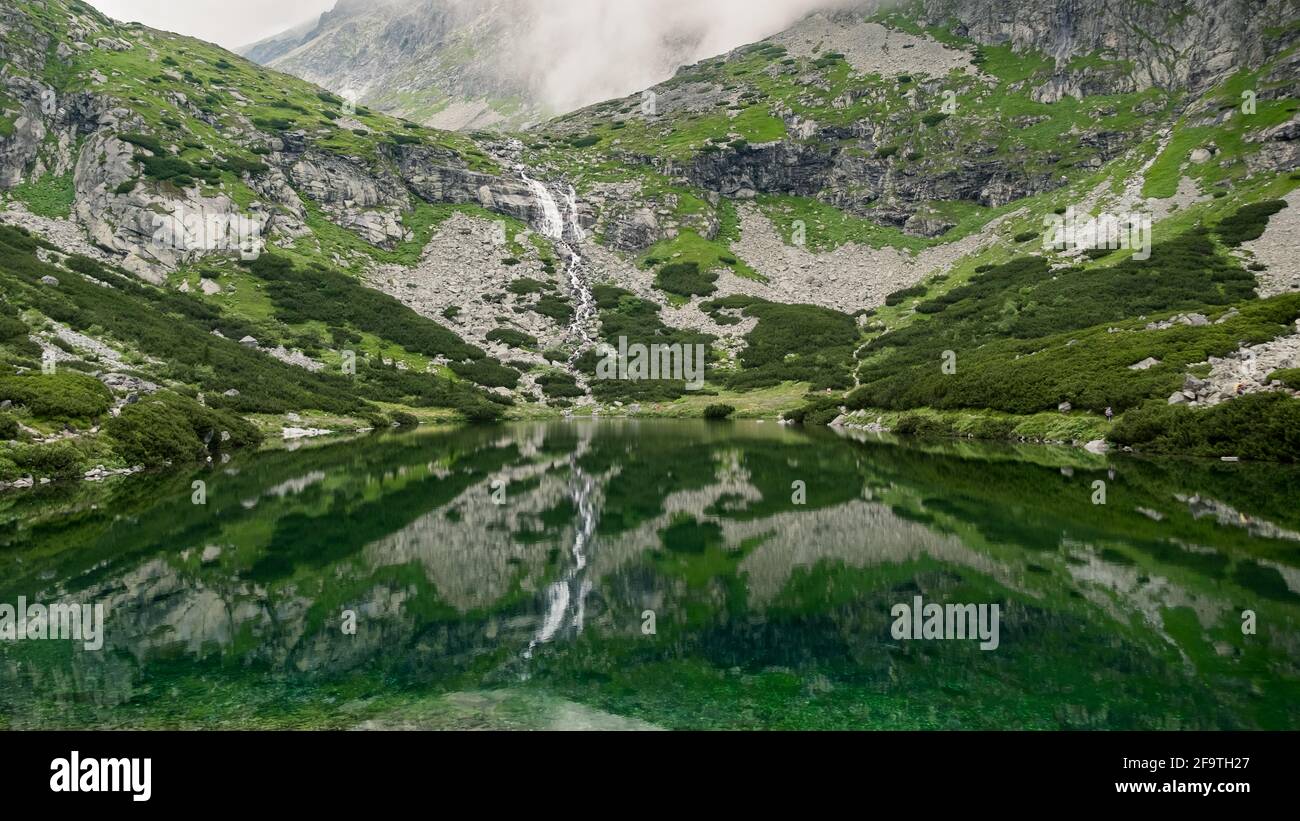 Mountain stream with view of rocky mountains and lake with transparent water Stock Photo