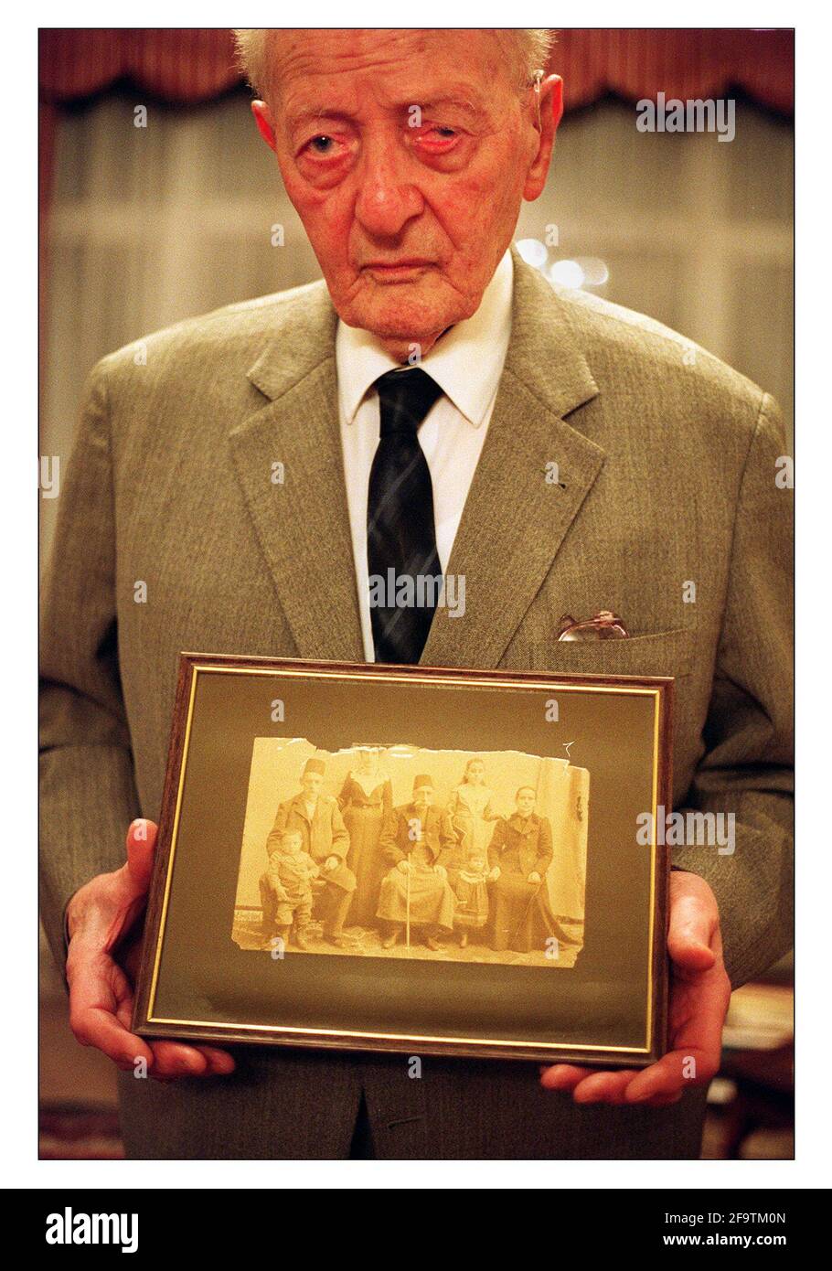 Armand Keshishian, Holocast Survivor January 2001 in his home in Willesden London. He is holding a photograph of himself as a very young boy (left in pic) with his grandfather, mother, great grandfather, little sister aunt and grandmother. Stock Photo