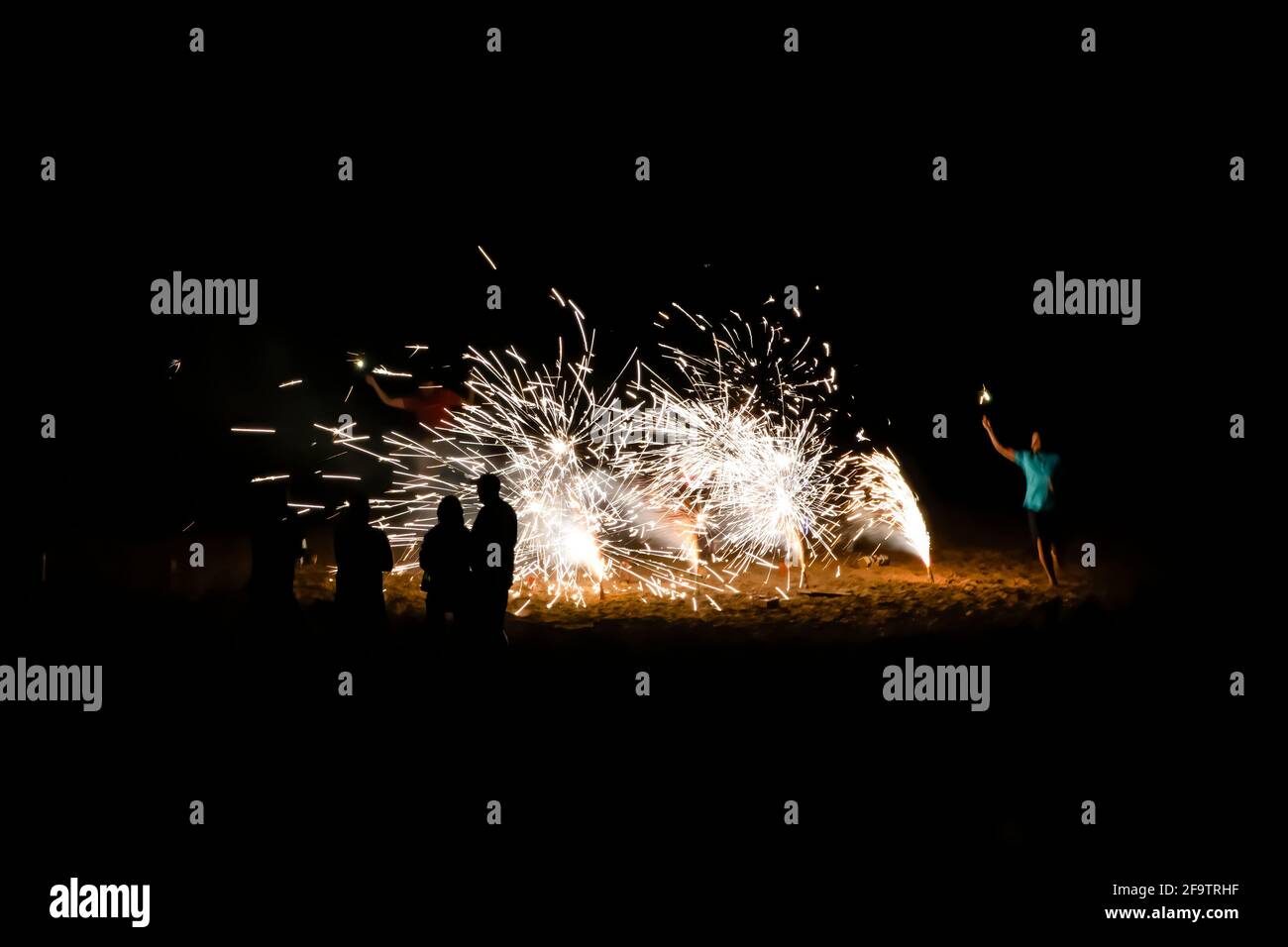 New Year’s Eve celebration on beach with fireworks on black background and people in silhouette. Stock Photo