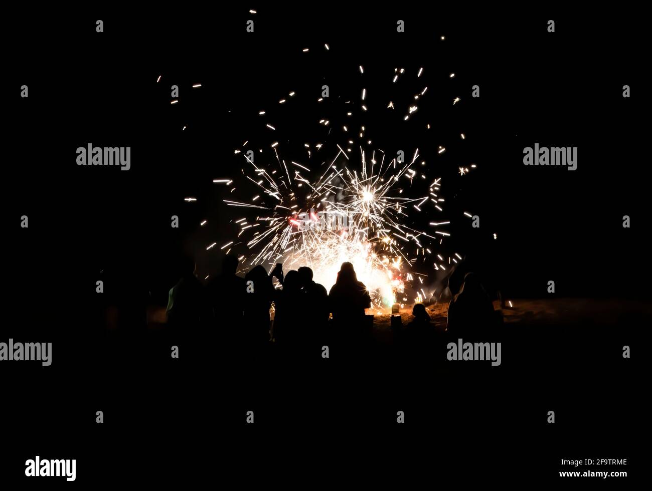 People take selfies and watch fireworks on beach with explosions of color against solid black night. Stock Photo