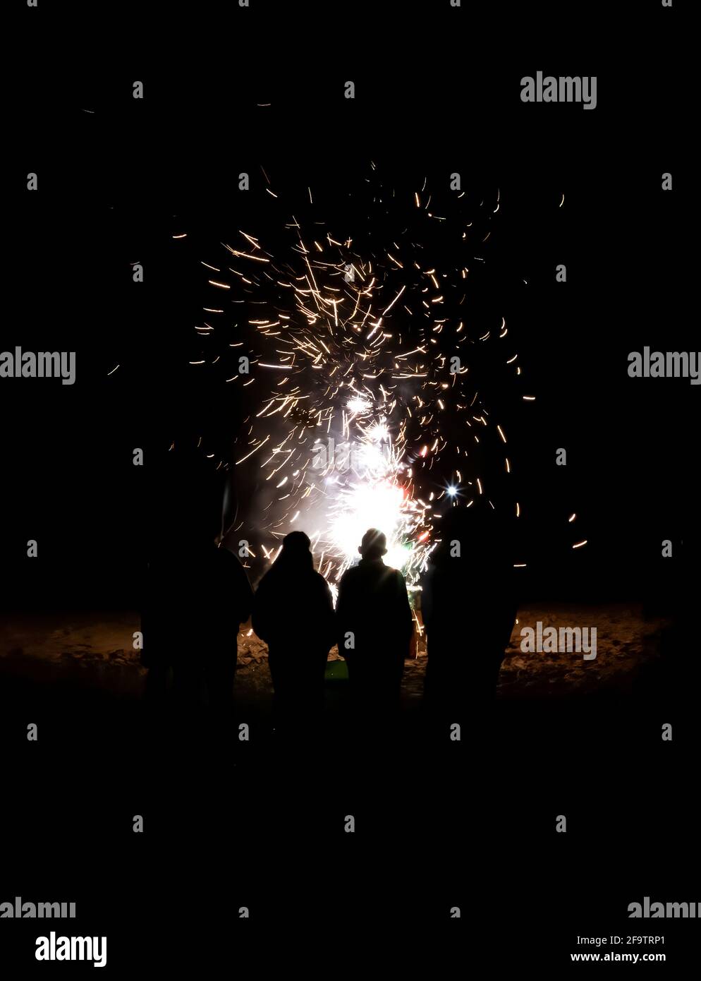 Group of people with back to camera in silhouette have a close up view of fireworks exploding on beach in black night. Stock Photo