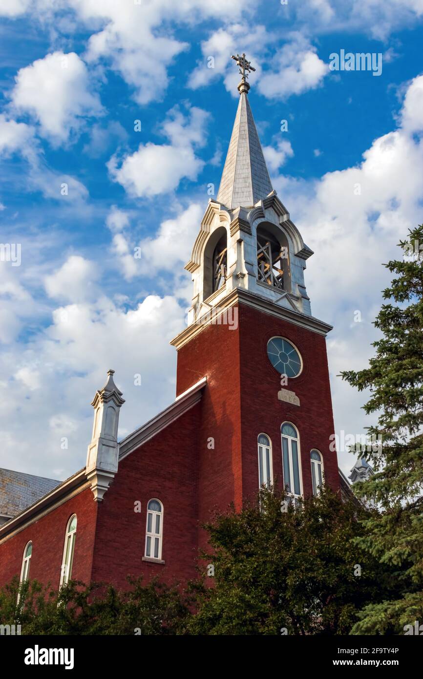 A red brick church with a silver coloured steeple - Country church with a bright blue sky and large fluffy white clouds Stock Photo