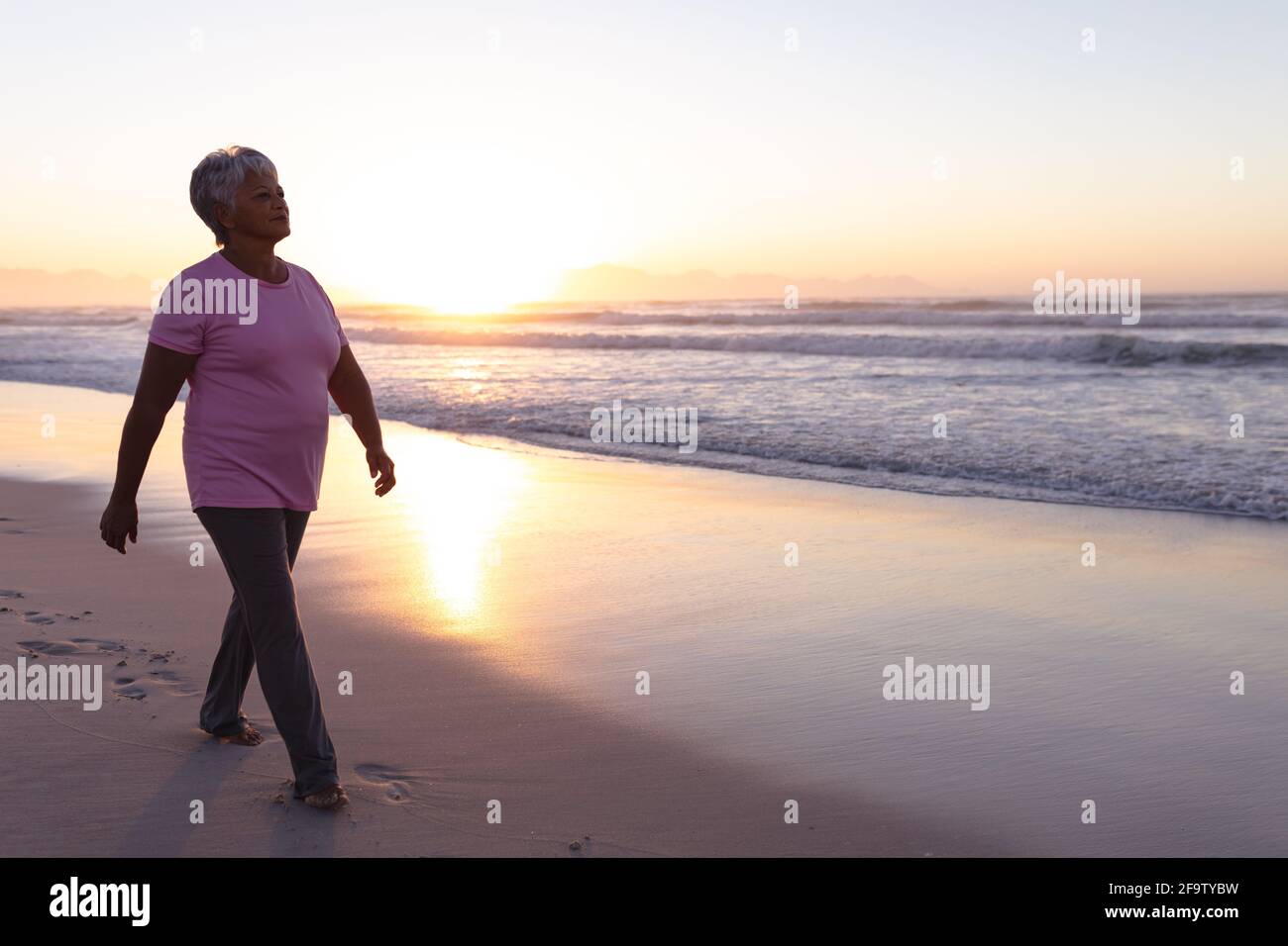 Senior african american woman walking on the beach during sunset Stock ...