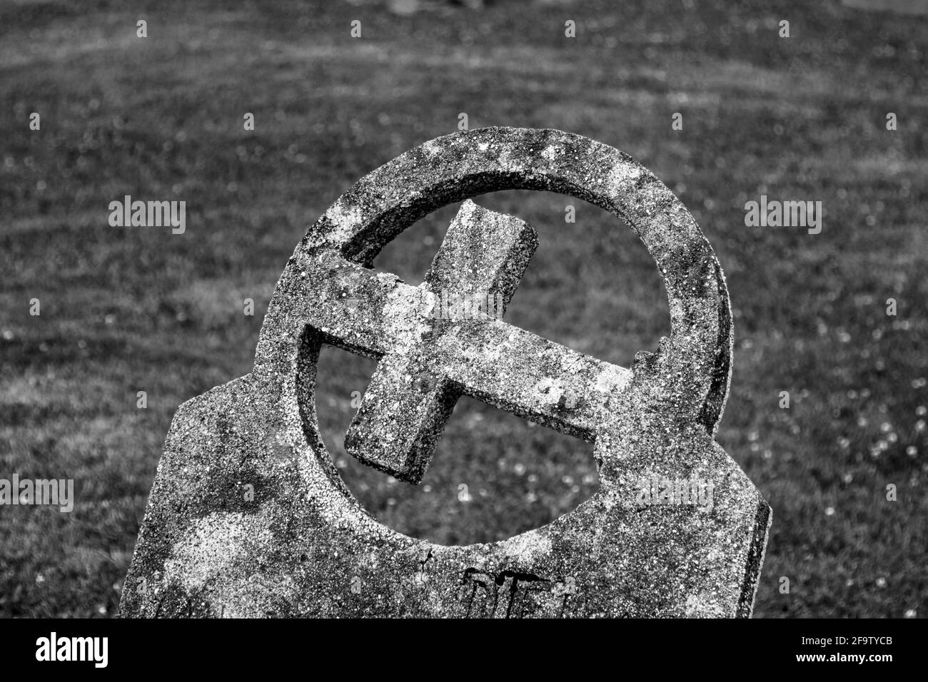 Stone grave with an angled cross inside a hollow circle - grass in the background Stock Photo