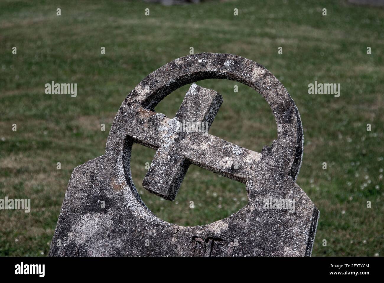 Headstone with an angled cross inside a hollow circle - grass in the background Stock Photo