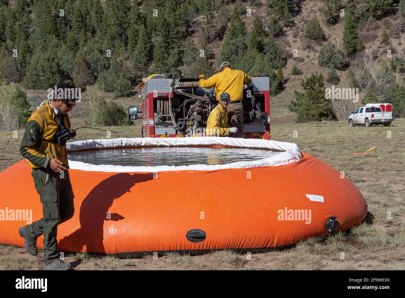 Forest Service fire fighters working a fire in New Mexico, a large orange portable water tank in the foreground. Stock Photo