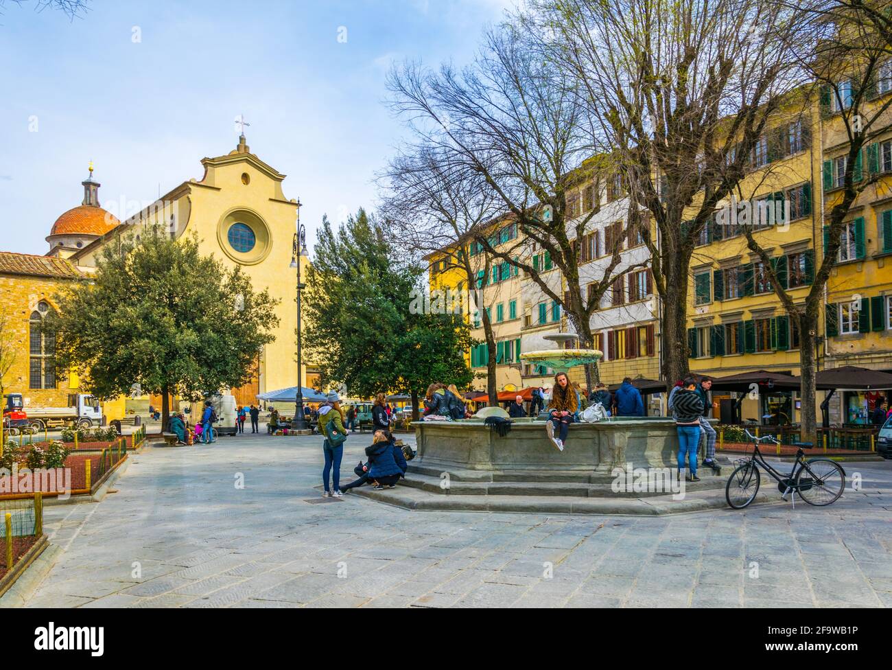FLORENCE, ITALY, MARCH 15, 2016: a group of young people is sitting on a fountain in front of the church santo spirito in the italian city florence. Stock Photo
