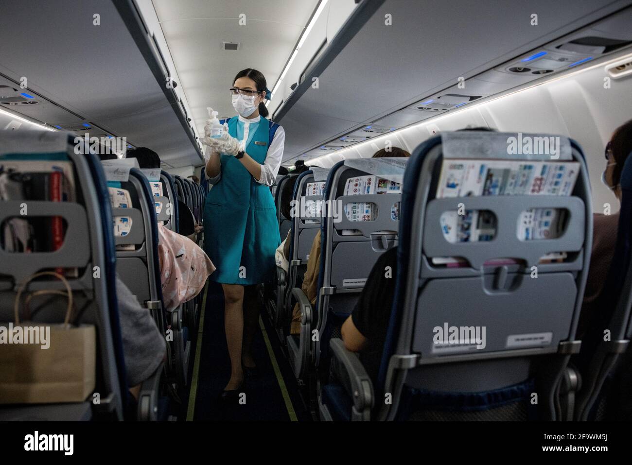 A member of Bangkok Airways cabin crew, wearing a face mask and protective glasses offers hand sanitiser to passengers on board a flight from Bangkok Suvarnabhumi Airport to Koh Samui, Thailand on March 8, 2021 during the global covid-19 pandemic. Stock Photo